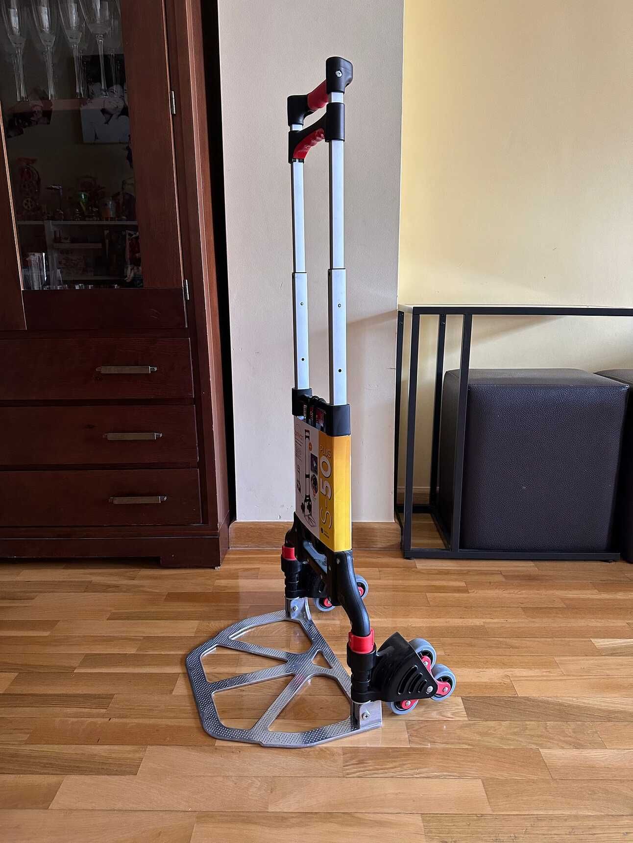 Una carretilla que tiene la base plegable y el mango extensible, así como tres ruedas pequeñas en lugar de cada rueda lateral